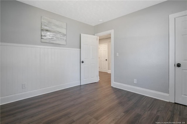 unfurnished bedroom with wainscoting, a textured ceiling, baseboards, and wood finished floors