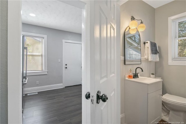 bathroom with toilet, wood finished floors, visible vents, vanity, and baseboards