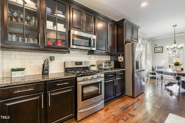 kitchen with decorative backsplash, appliances with stainless steel finishes, dark wood-type flooring, ornamental molding, and dark stone countertops