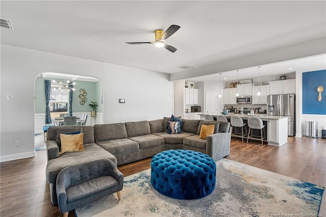 living area with arched walkways, dark wood-type flooring, ceiling fan with notable chandelier, and visible vents