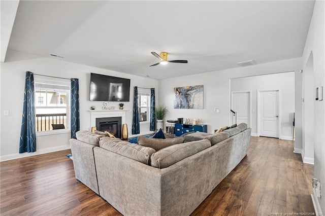 living area with visible vents, baseboards, dark wood finished floors, and a glass covered fireplace