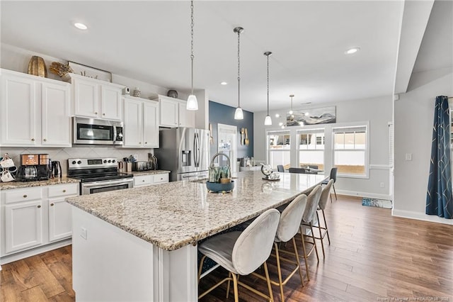 kitchen with white cabinets, decorative backsplash, a large island, appliances with stainless steel finishes, and wood finished floors