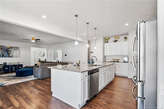 kitchen with arched walkways, light stone counters, open floor plan, stainless steel appliances, and a sink