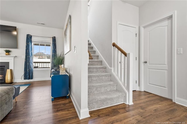 stairs with wood finished floors, a glass covered fireplace, visible vents, and baseboards