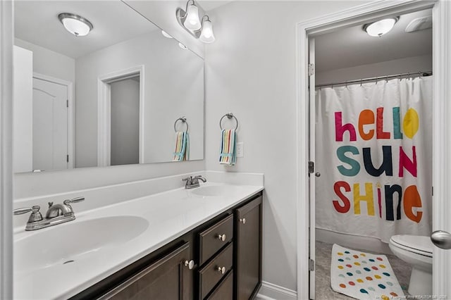 full bath with double vanity, baseboards, toilet, and a sink