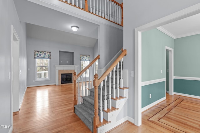 stairs featuring baseboards, a tiled fireplace, a towering ceiling, ornamental molding, and wood finished floors