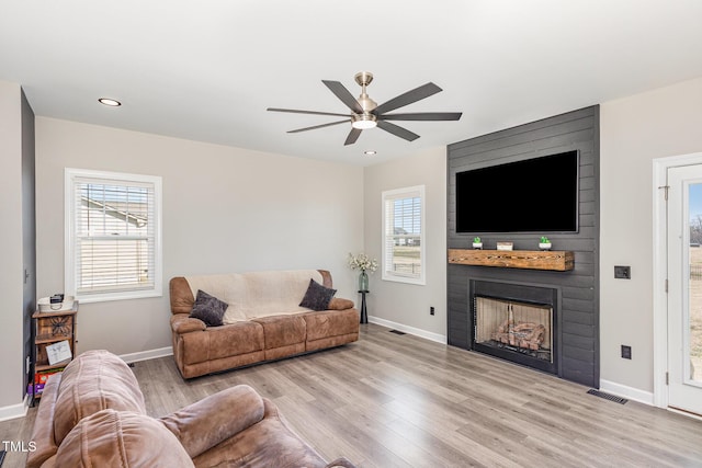 living area with light wood-type flooring, a large fireplace, and baseboards