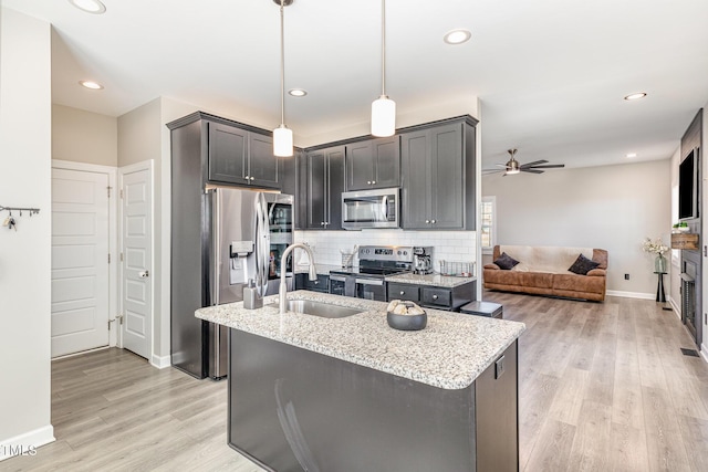 kitchen featuring backsplash, appliances with stainless steel finishes, a sink, light stone countertops, and light wood-type flooring