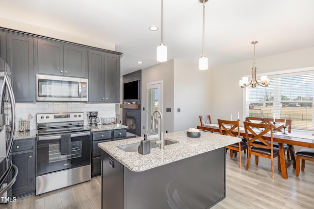 kitchen featuring light wood-style flooring, stainless steel appliances, a sink, backsplash, and light stone countertops