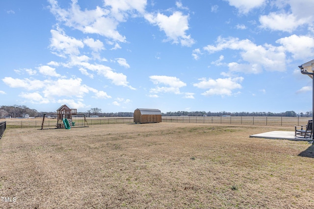 view of yard with a rural view, a playground, a fenced backyard, a storage shed, and an outdoor structure