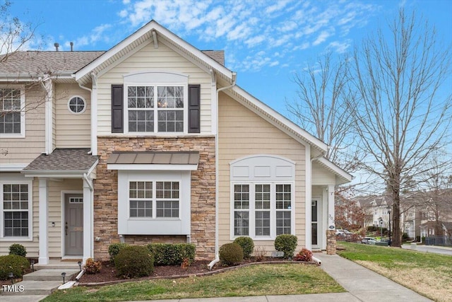 view of front of house featuring a front yard, stone siding, and roof with shingles