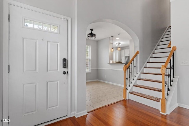 entrance foyer with stairs, wood finished floors, arched walkways, and baseboards