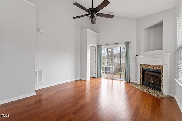 unfurnished living room with wood finished floors, visible vents, baseboards, a tile fireplace, and a towering ceiling