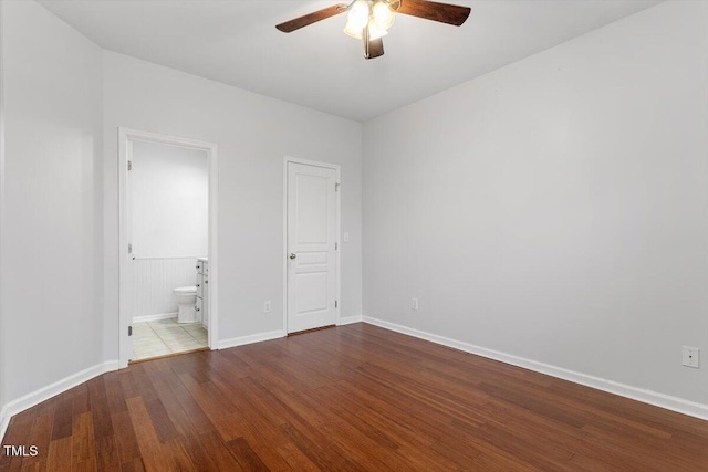 unfurnished bedroom featuring ceiling fan, ensuite bathroom, baseboards, and wood finished floors