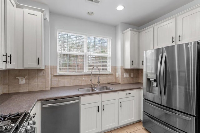 kitchen with decorative backsplash, stainless steel appliances, light tile patterned flooring, white cabinetry, and a sink