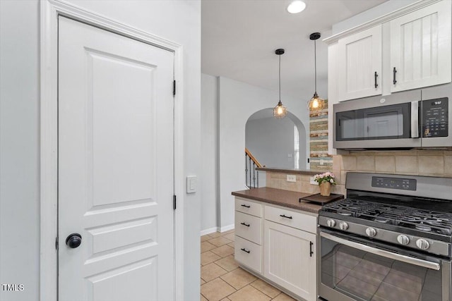 kitchen with white cabinets, appliances with stainless steel finishes, pendant lighting, dark countertops, and tasteful backsplash