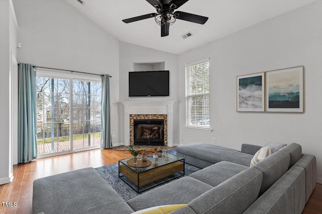 living area featuring visible vents, ceiling fan, vaulted ceiling, a fireplace, and wood finished floors