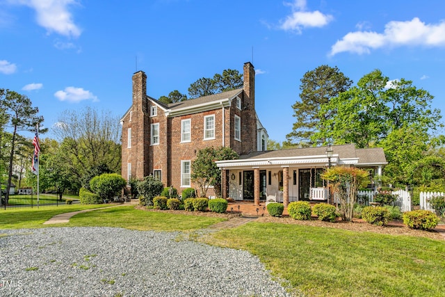 view of front of property with a porch, fence, a front lawn, brick siding, and a chimney