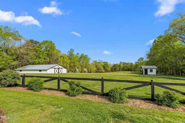 view of gate featuring a yard, an outdoor structure, fence, and a view of trees