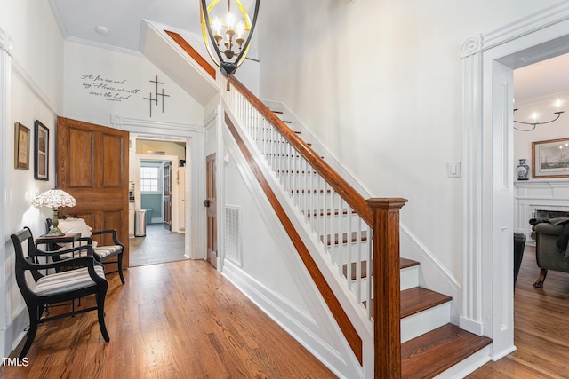 stairs featuring a notable chandelier, baseboards, crown molding, visible vents, and wood finished floors