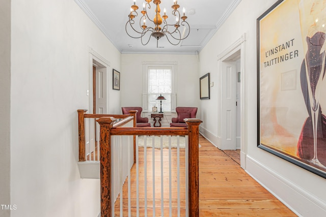 corridor with ornamental molding, baseboards, light wood finished floors, and a chandelier