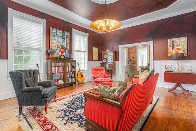 living area featuring a notable chandelier, crown molding, a wainscoted wall, a decorative wall, and wood finished floors