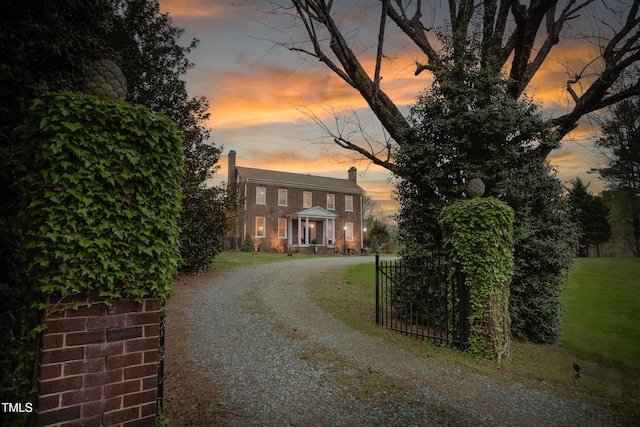 view of front of house featuring gravel driveway, a chimney, a gate, and a front lawn