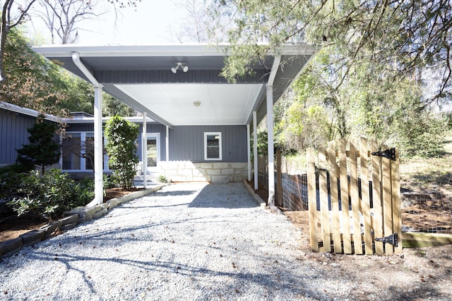 view of front of home with stone siding, gravel driveway, a carport, fence, and board and batten siding