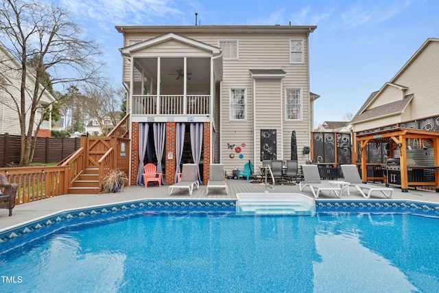 rear view of property featuring a fenced in pool, fence, stairs, a deck, and a sunroom