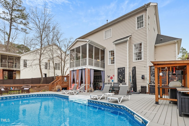 rear view of property with a wooden deck, a patio, a fenced in pool, and a sunroom