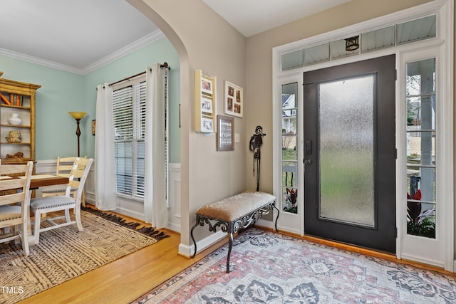 foyer with baseboards, arched walkways, wood finished floors, and ornamental molding