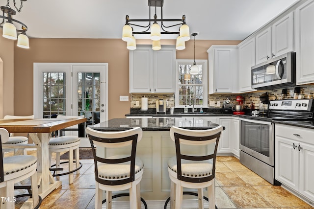 kitchen featuring a kitchen island, decorative backsplash, stainless steel appliances, white cabinetry, and a sink