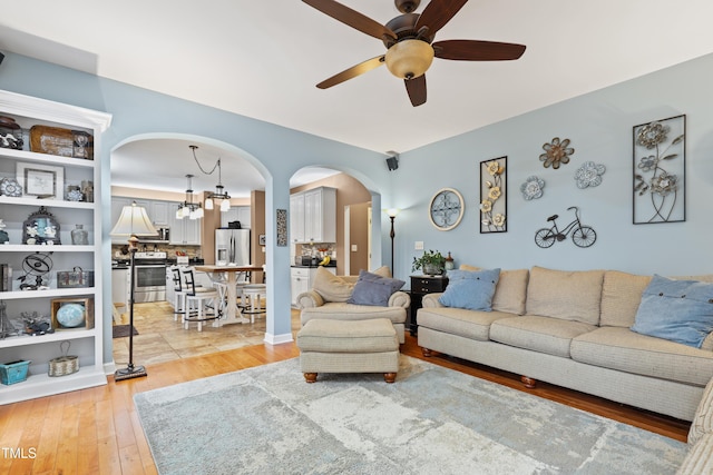 living room with arched walkways, light wood-style flooring, and ceiling fan with notable chandelier