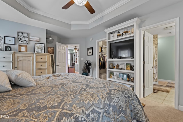 carpeted bedroom with tile patterned floors, a walk in closet, a raised ceiling, and crown molding