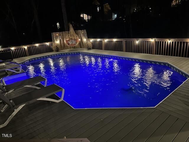 pool at twilight with a fenced in pool and a wooden deck