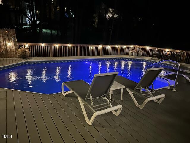 pool at twilight with a fenced in pool and a wooden deck