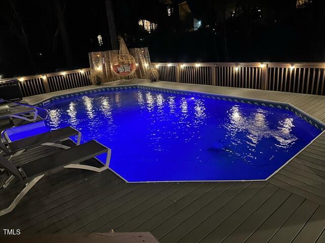 pool at night with a fenced in pool and a deck