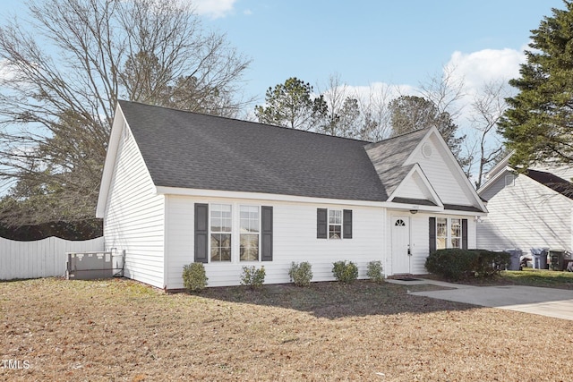 traditional-style home with a shingled roof, a front lawn, and fence