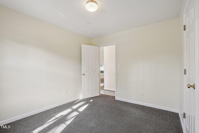 unfurnished bedroom with dark carpet, a textured ceiling, and baseboards