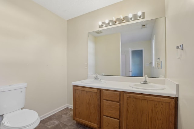 bathroom with double vanity, a sink, toilet, and baseboards