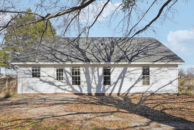 rear view of house featuring a shingled roof and fence