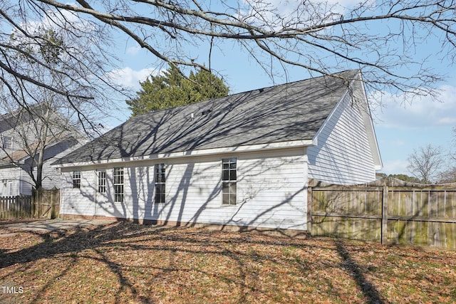 view of side of home with a shingled roof and fence