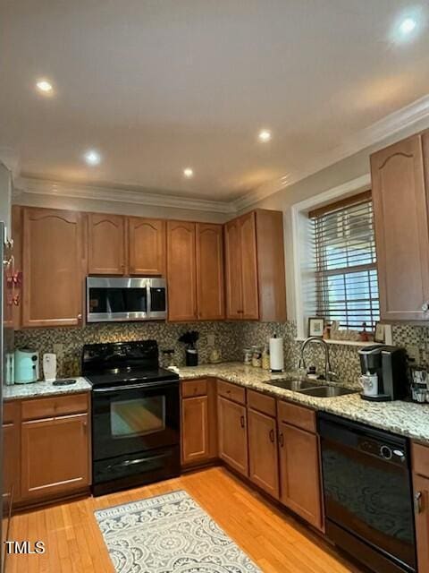 kitchen with black appliances, a sink, light wood-style floors, crown molding, and light stone countertops
