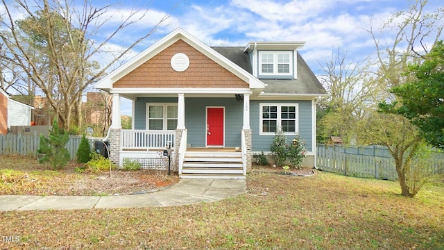 bungalow-style house featuring covered porch, fence, and a front lawn