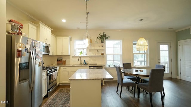 kitchen with stainless steel appliances, tasteful backsplash, ornamental molding, a kitchen island, and a sink