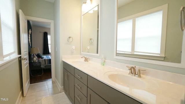 ensuite bathroom with double vanity, tile patterned flooring, baseboards, and a sink