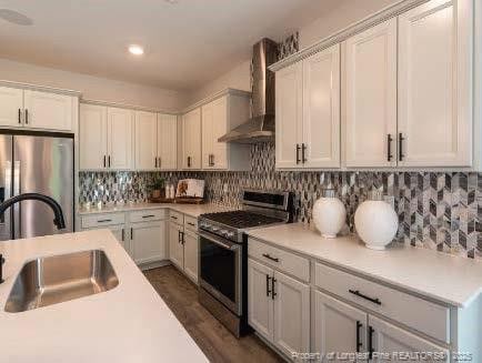 kitchen with tasteful backsplash, stainless steel appliances, light countertops, wall chimney range hood, and a sink