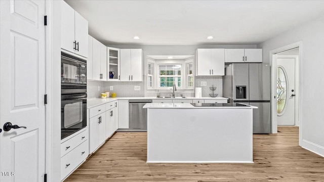 kitchen featuring black appliances, light wood finished floors, a sink, and a center island