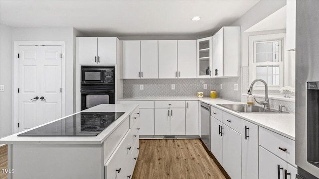 kitchen featuring white cabinets, light wood-style floors, backsplash, black appliances, and a sink