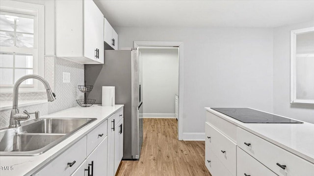 kitchen featuring black electric stovetop, a sink, white cabinets, light wood-type flooring, and backsplash